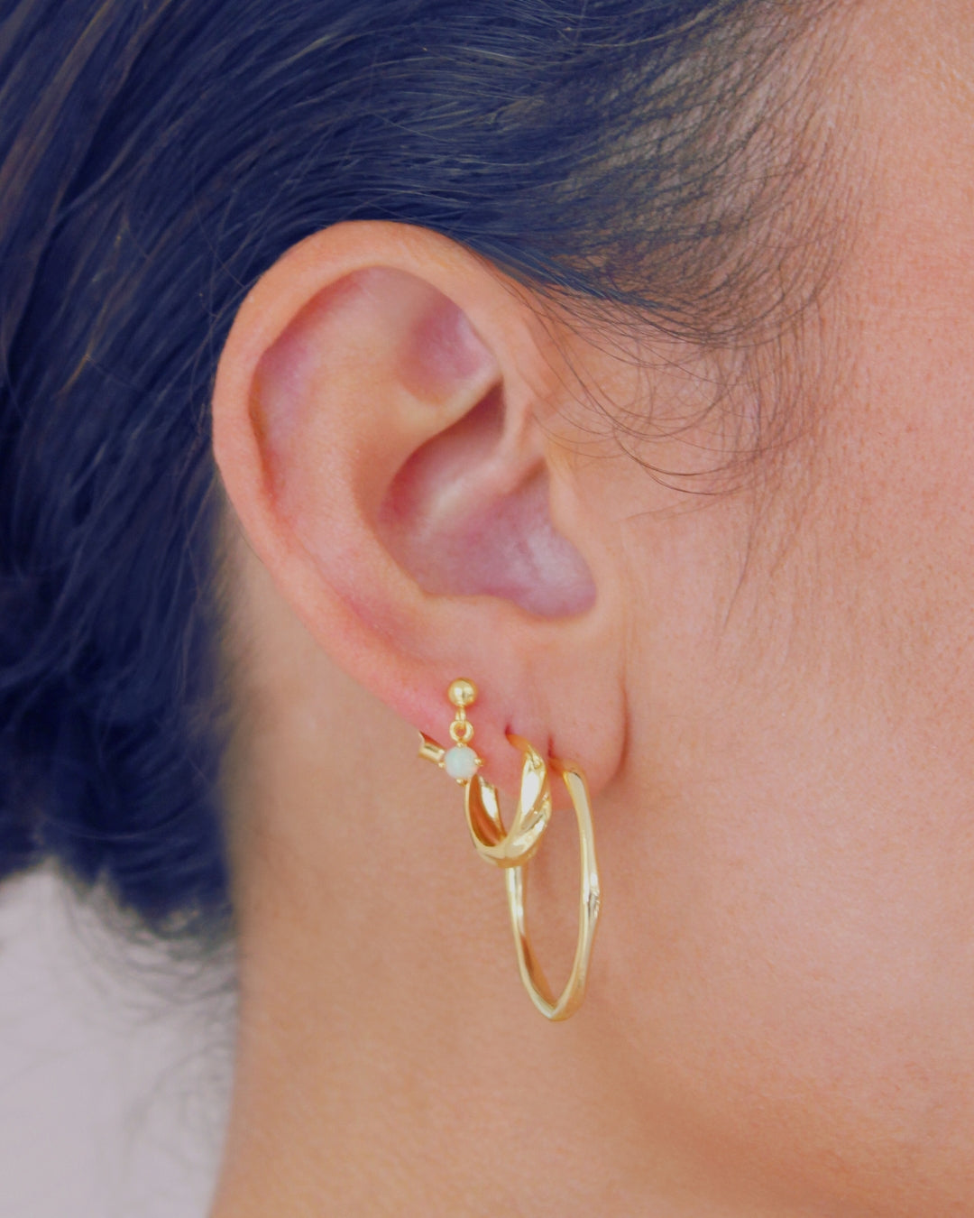 Gold drop stud earrings with a small gemstone worn by a person with black air.