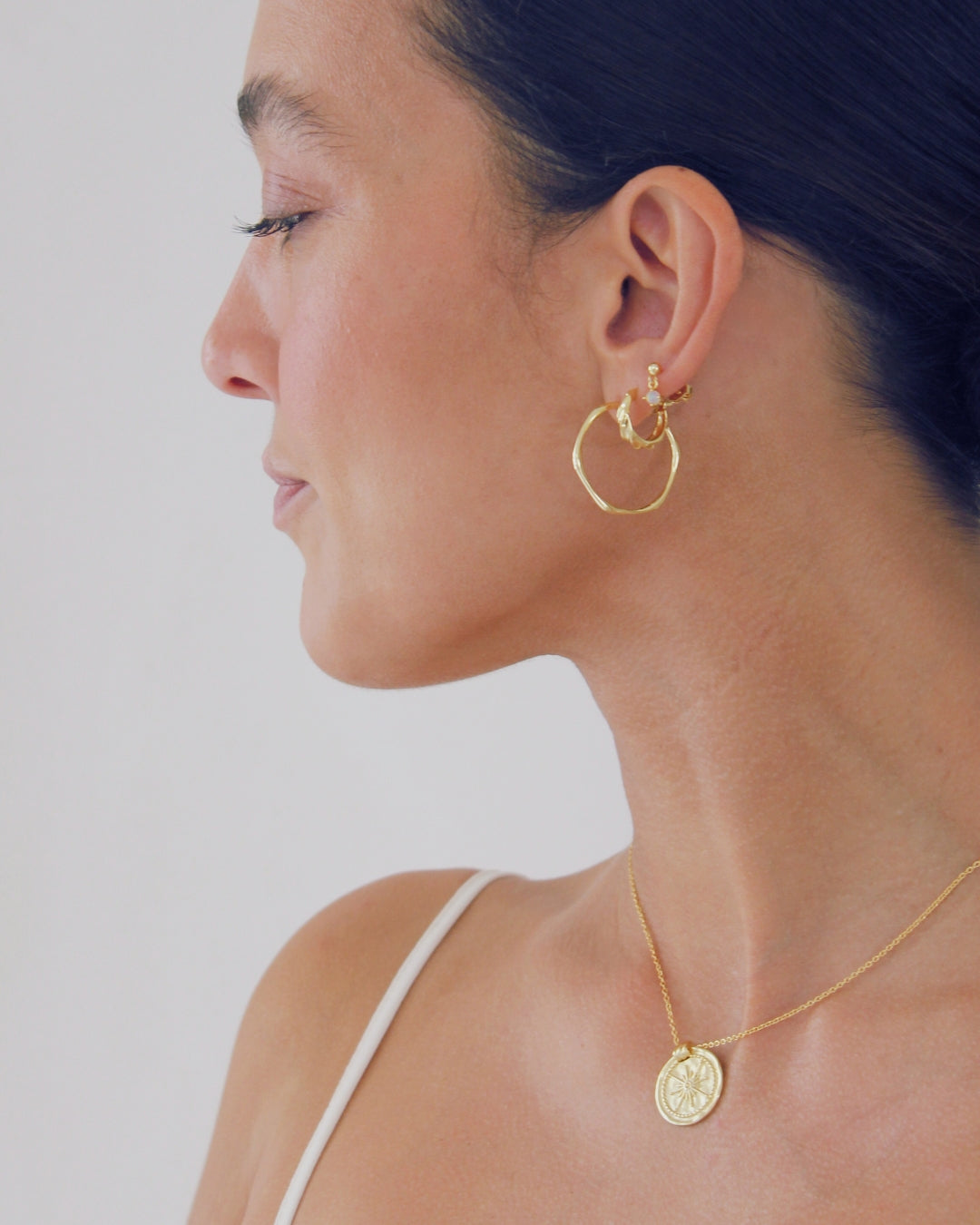 Woman wearing gold hoop earrings and necklace against a plain background
