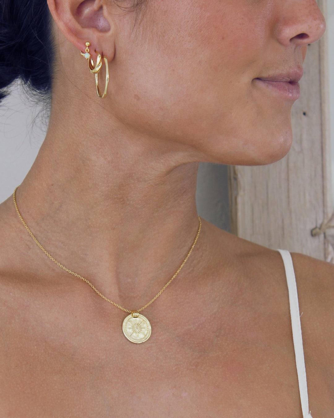 Close-up of a person wearing gold earrings and a gold necklace with a coin pendant.