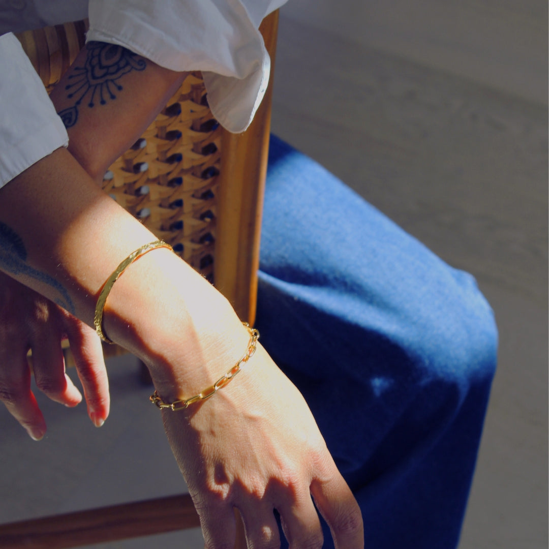 Close-up of a person's wrist wearing gold bracelets with a blurred background.