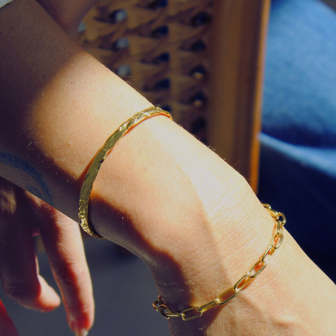 Close-up of a wrist wearing two gold bracelets with a blurred background.