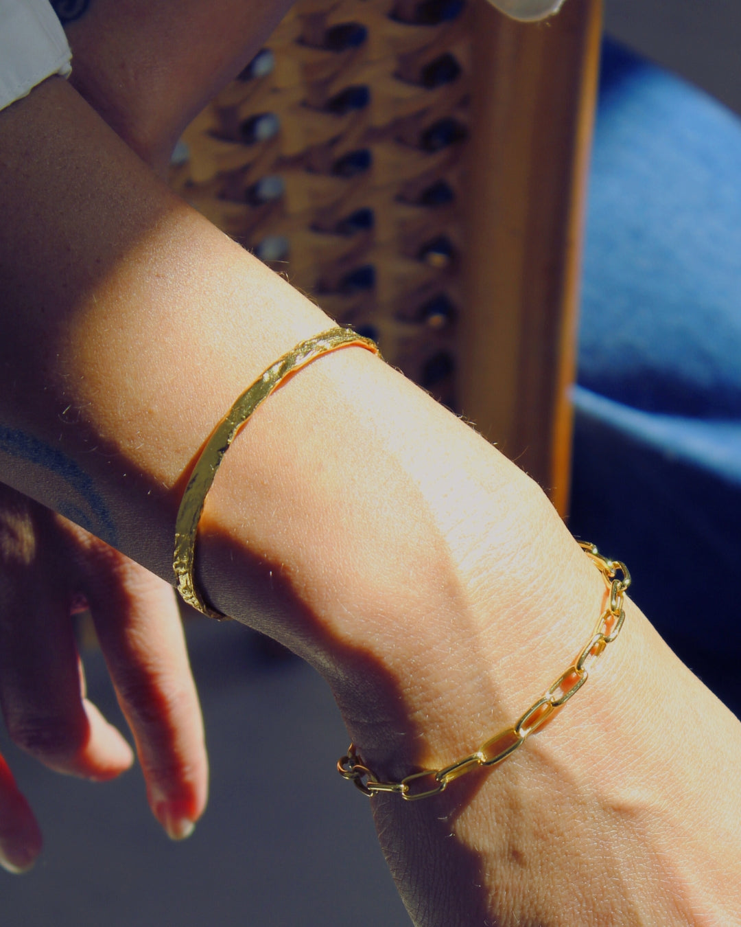 Close-up of a wrist wearing two gold bracelets with a blurred background.