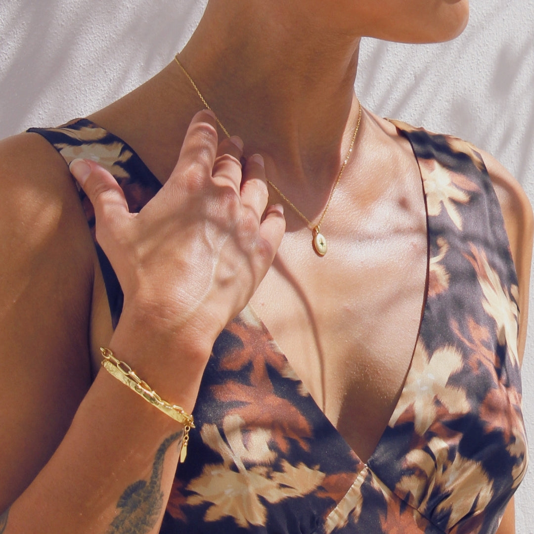 Woman wearing a floral dress with a gold necklace and the Avalon cuff bracelet against a neutral background