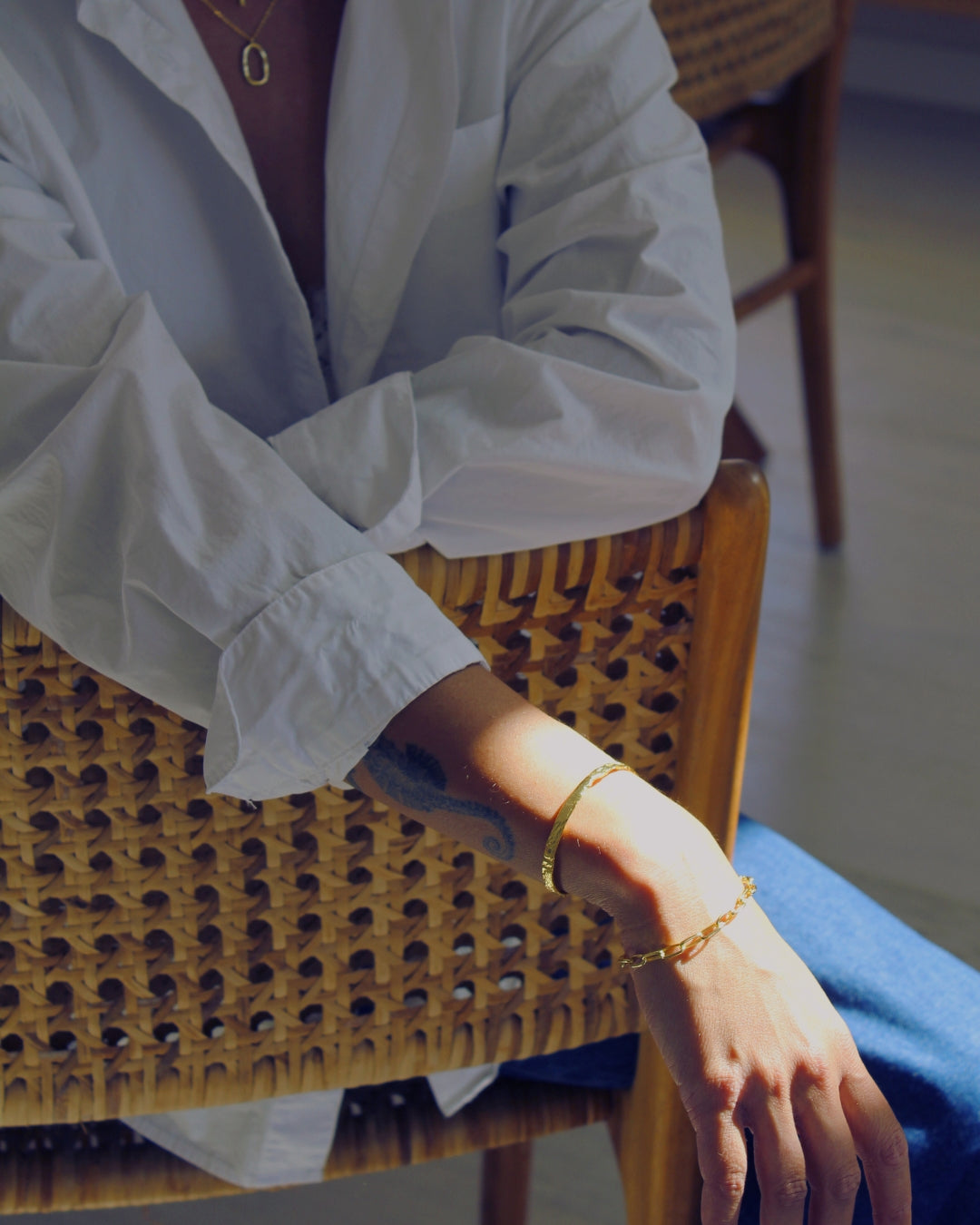 Person wearing a white shirt and blue jeans sitting on a wicker chair with two bracelets one of which is the Avalon Cuff