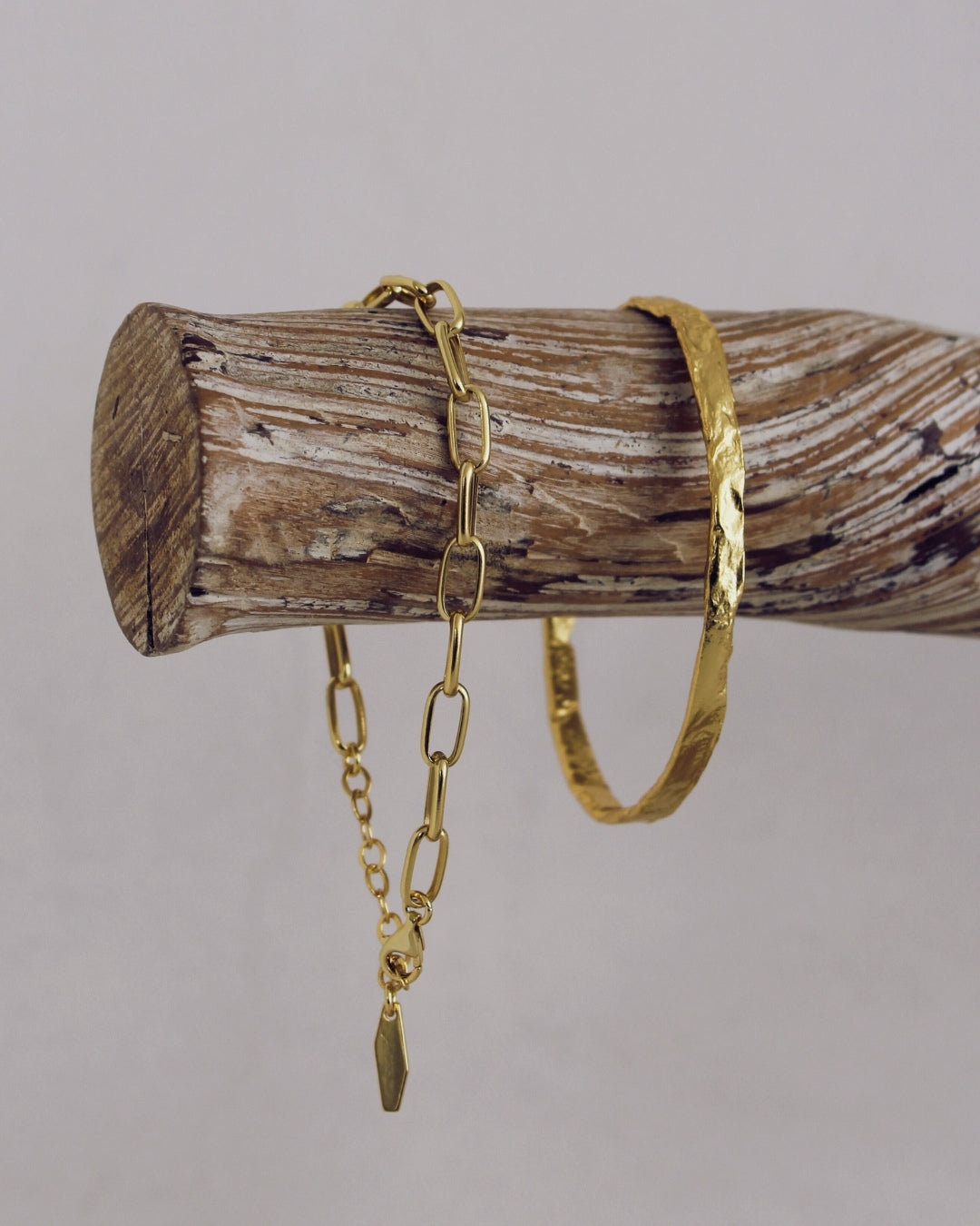 Gold chain bracelet and Avalon Cuff on a wooden log against a grey background