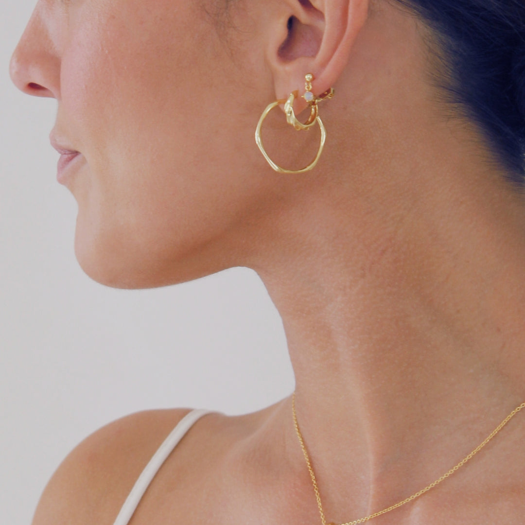 Close-up of a person wearing gold hoop earrings and a necklace with a coin pendant.