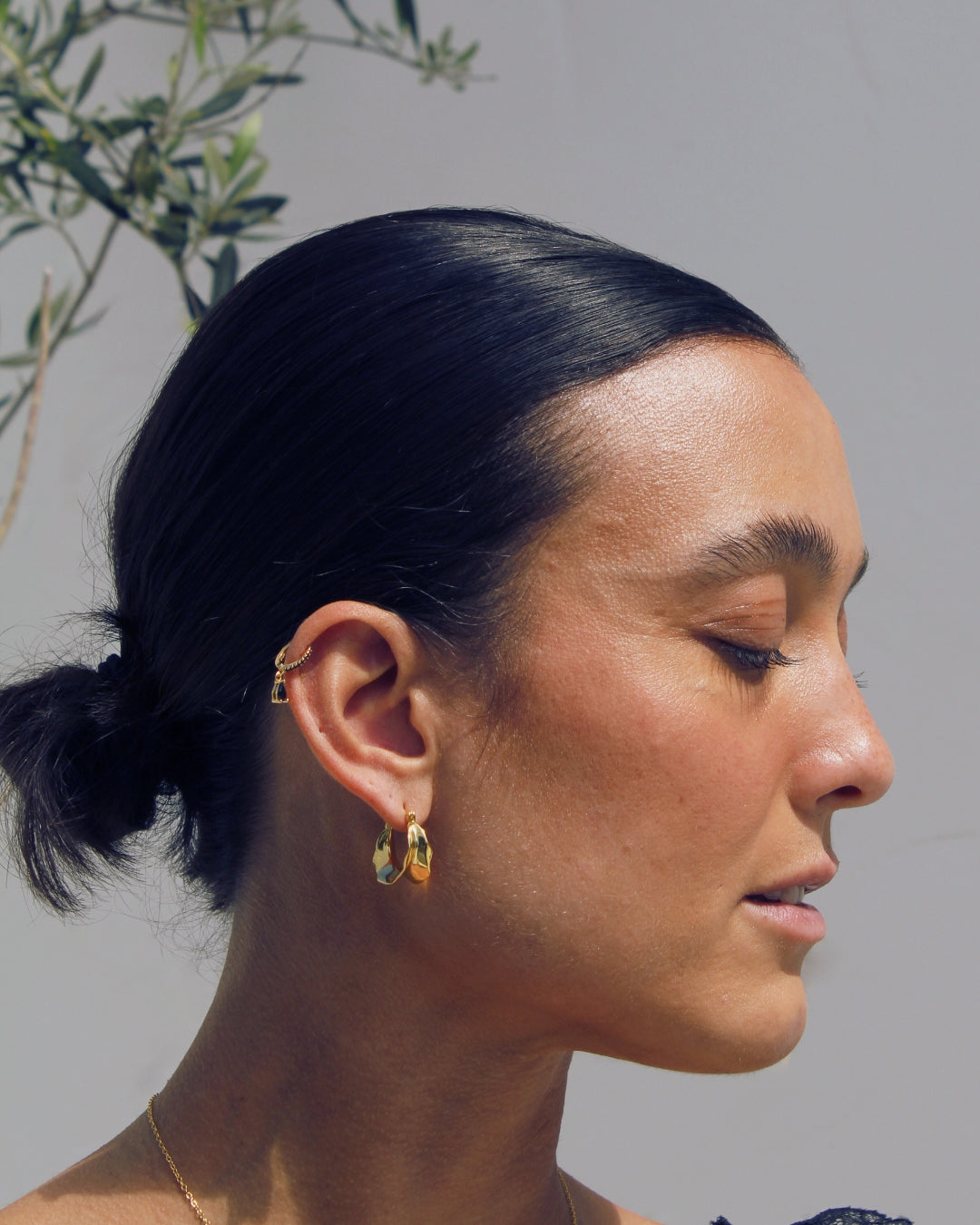 Close-up of a person with a ponytail and gold earrings against a neutral background