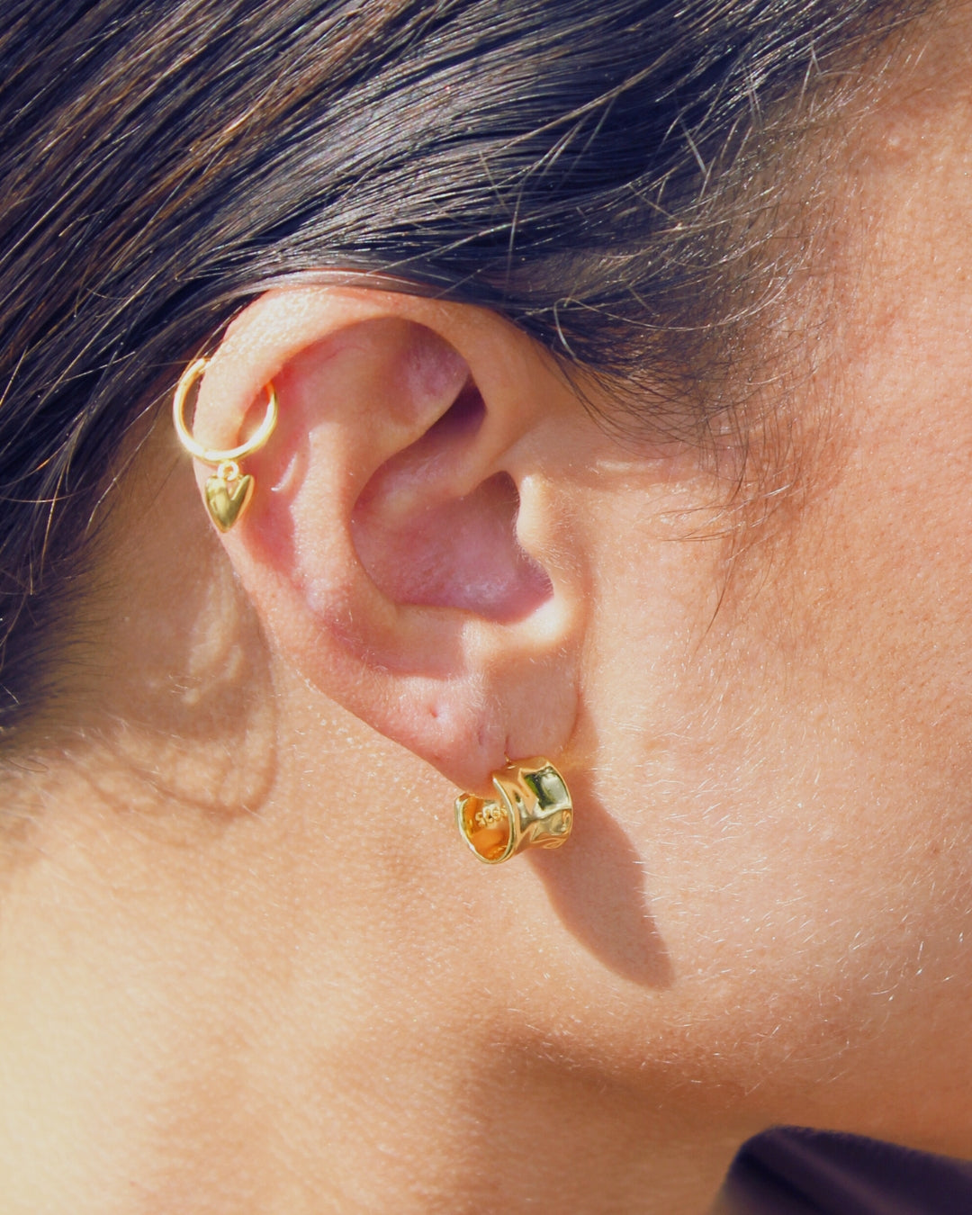 Close-up of an ear wearing gold hoop earrings with a blurred background