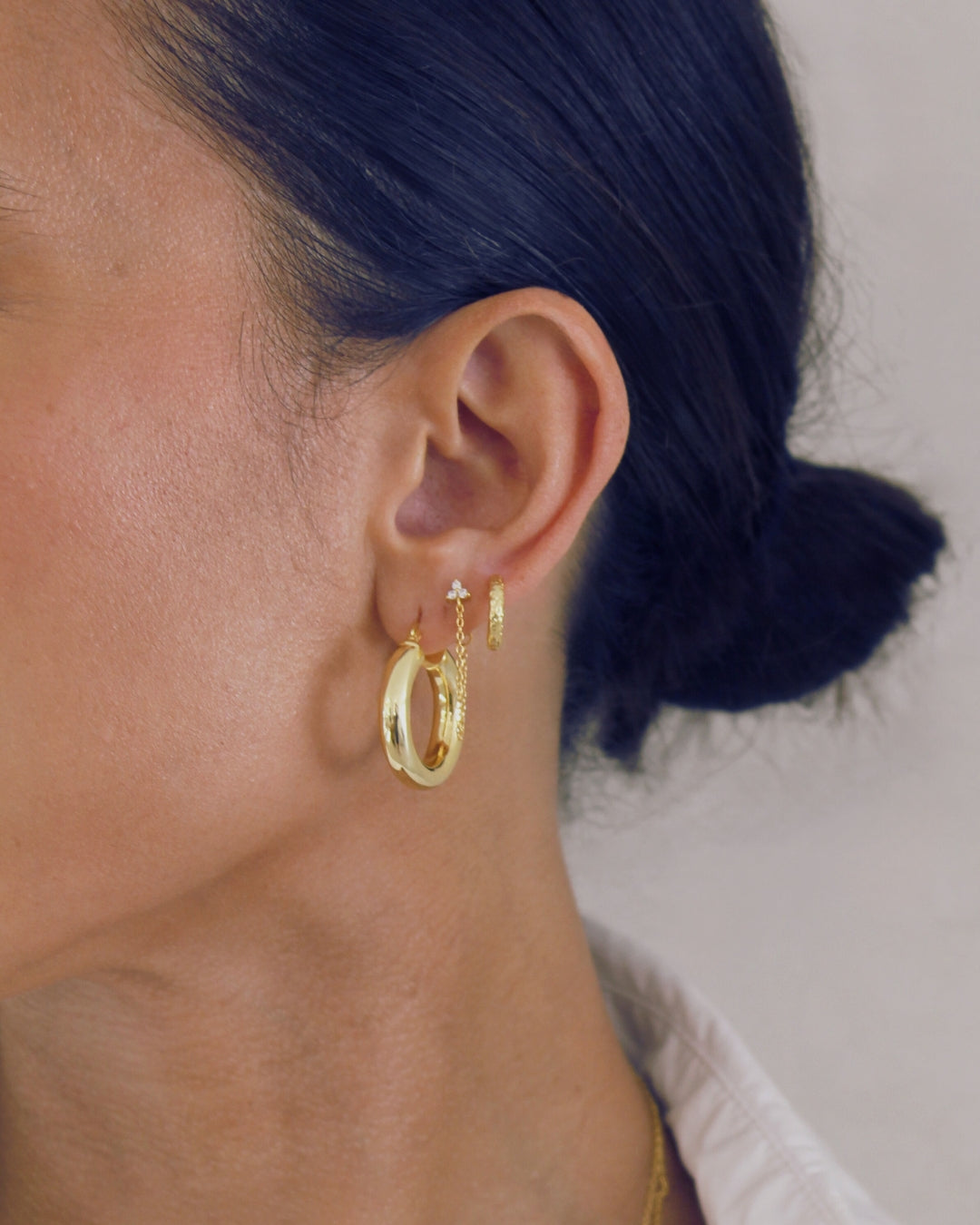 Close-up of an ear wearing gold hoop earrings and the Freya chain earring with a blurred background