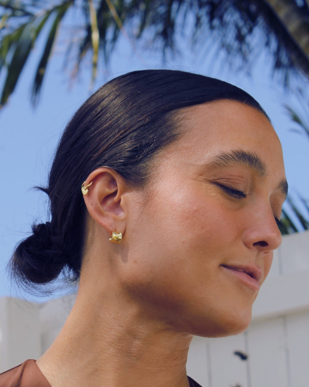 Close-up of a women wearing gold earrings with a blurred outdoor background