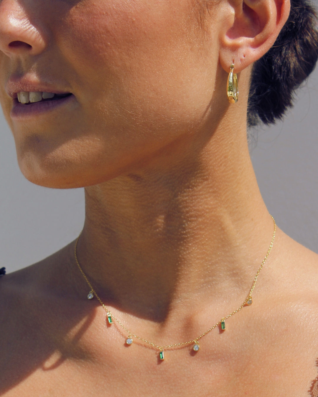 Close-up of a person wearing a gold necklace and earrings against a neutral background