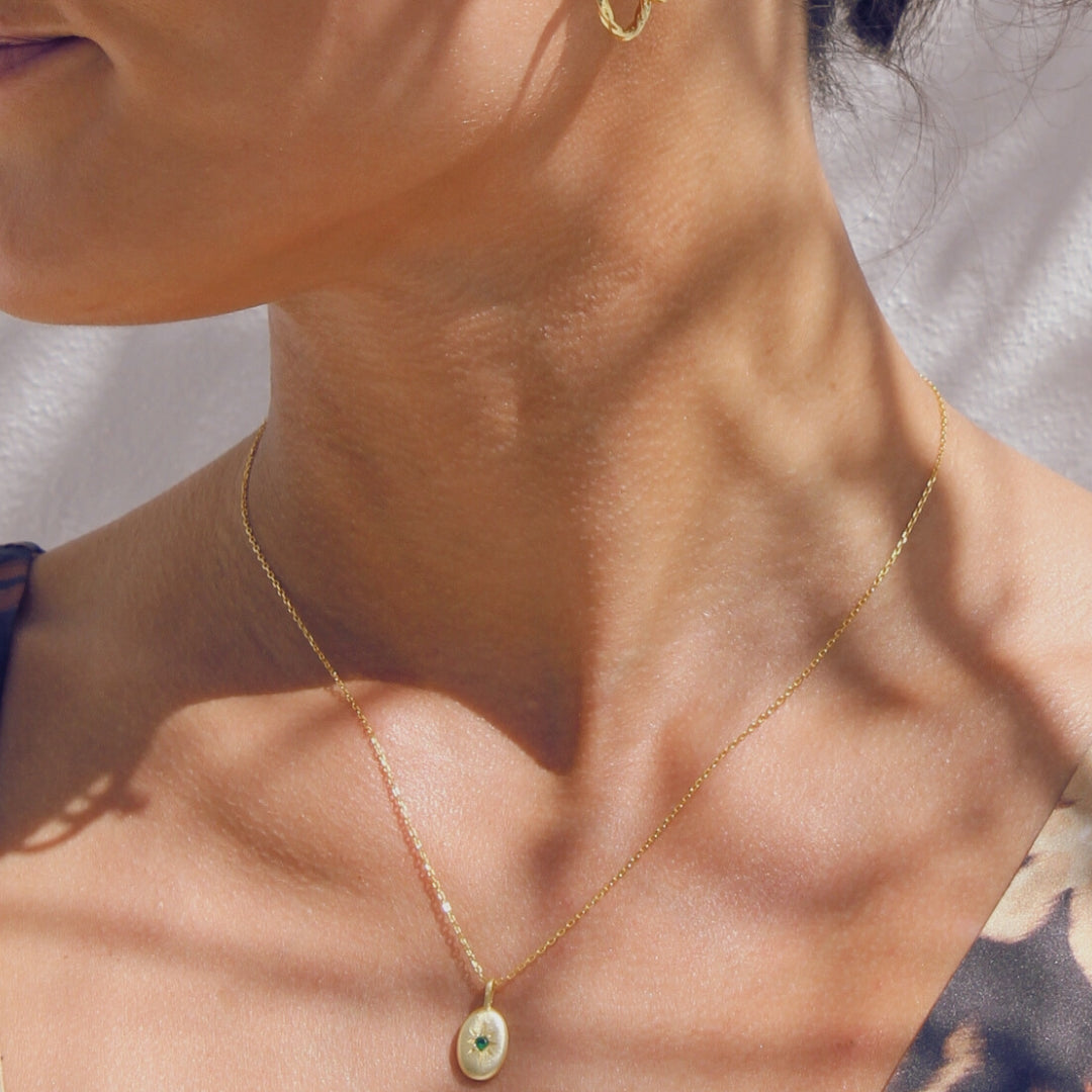 Close-up of a woman wearing gold hoop earrings and a gold necklace with a pendant.