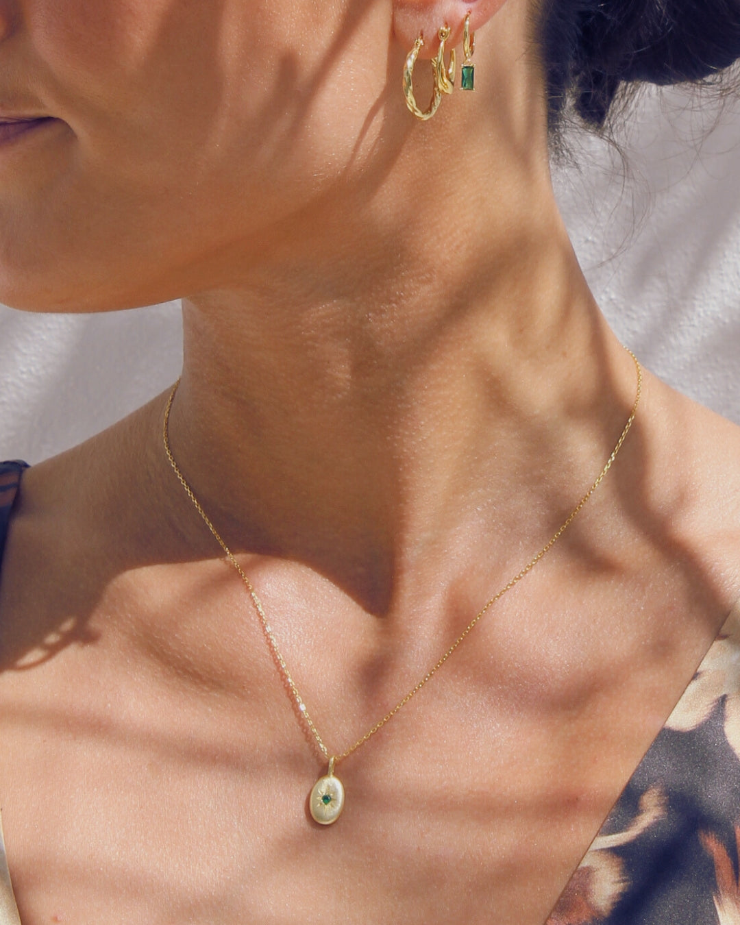 Close-up of a woman wearing gold hoop earrings and a gold necklace with a pendant.