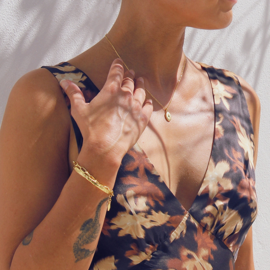 Woman wearing a floral dress with gold jewelry against a neutral background