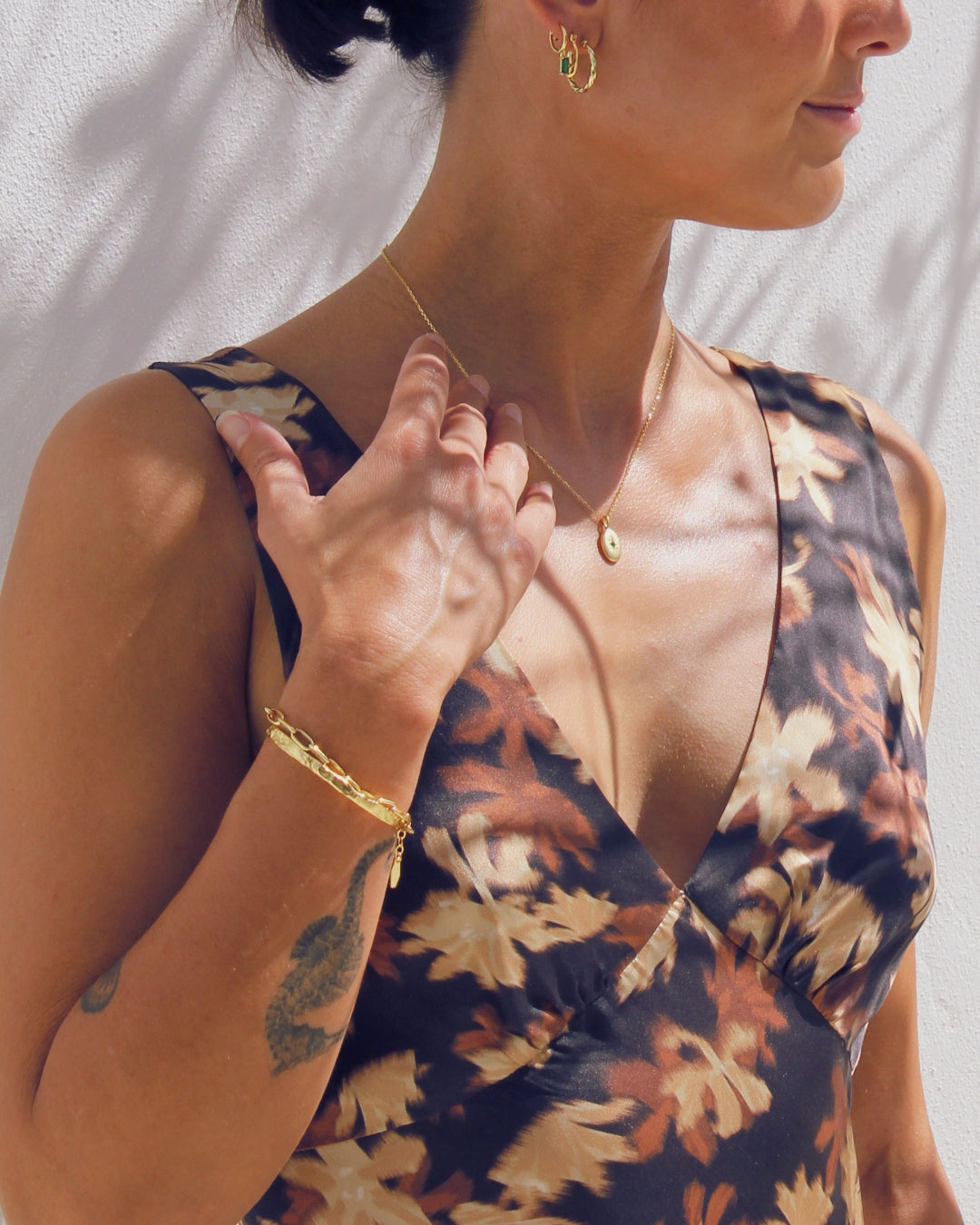 Woman wearing a floral dress with gold jewelry against a neutral background