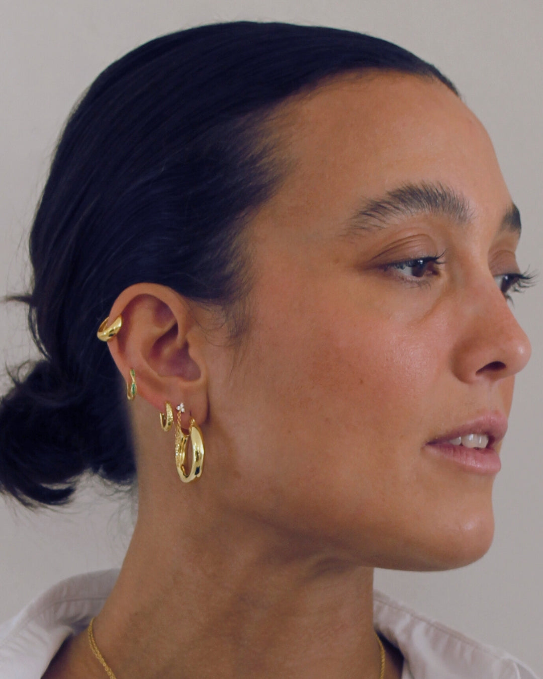 Close-up of a person wearing gold earrings in a stack with a neutral background