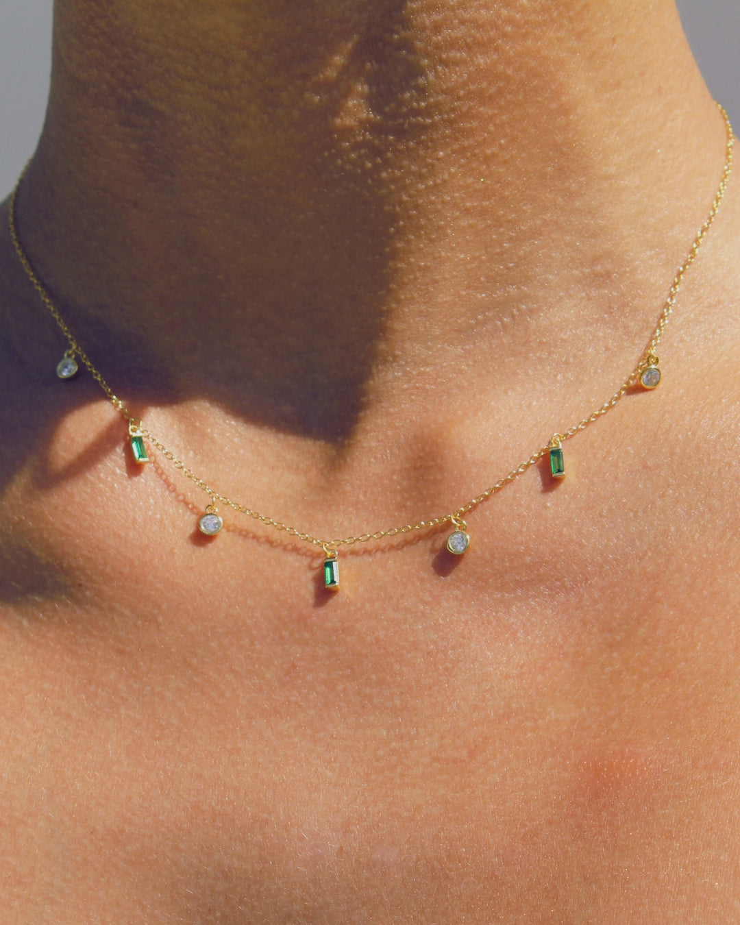 18k Gold necklace with green and clear gemstones pendants close up on a woman's neck