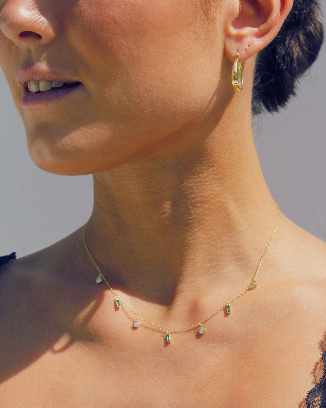 Close-up of a person wearing a delicate gold necklace with small gemstones against a neutral background.