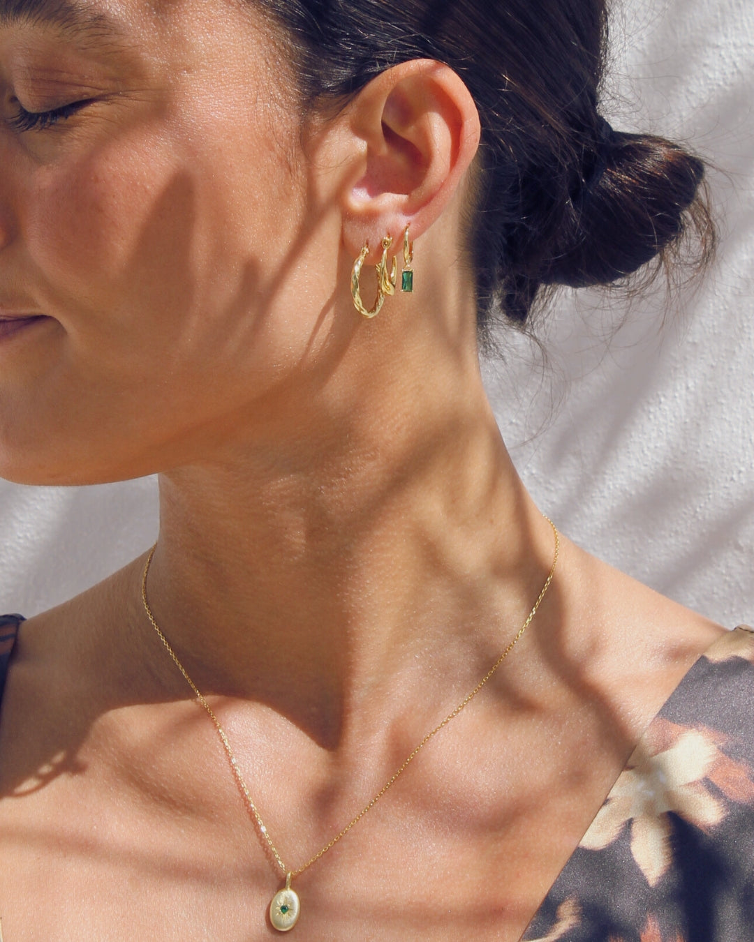 Close-up of a woman wearing gold hoop earrings and a necklace with a neutral background