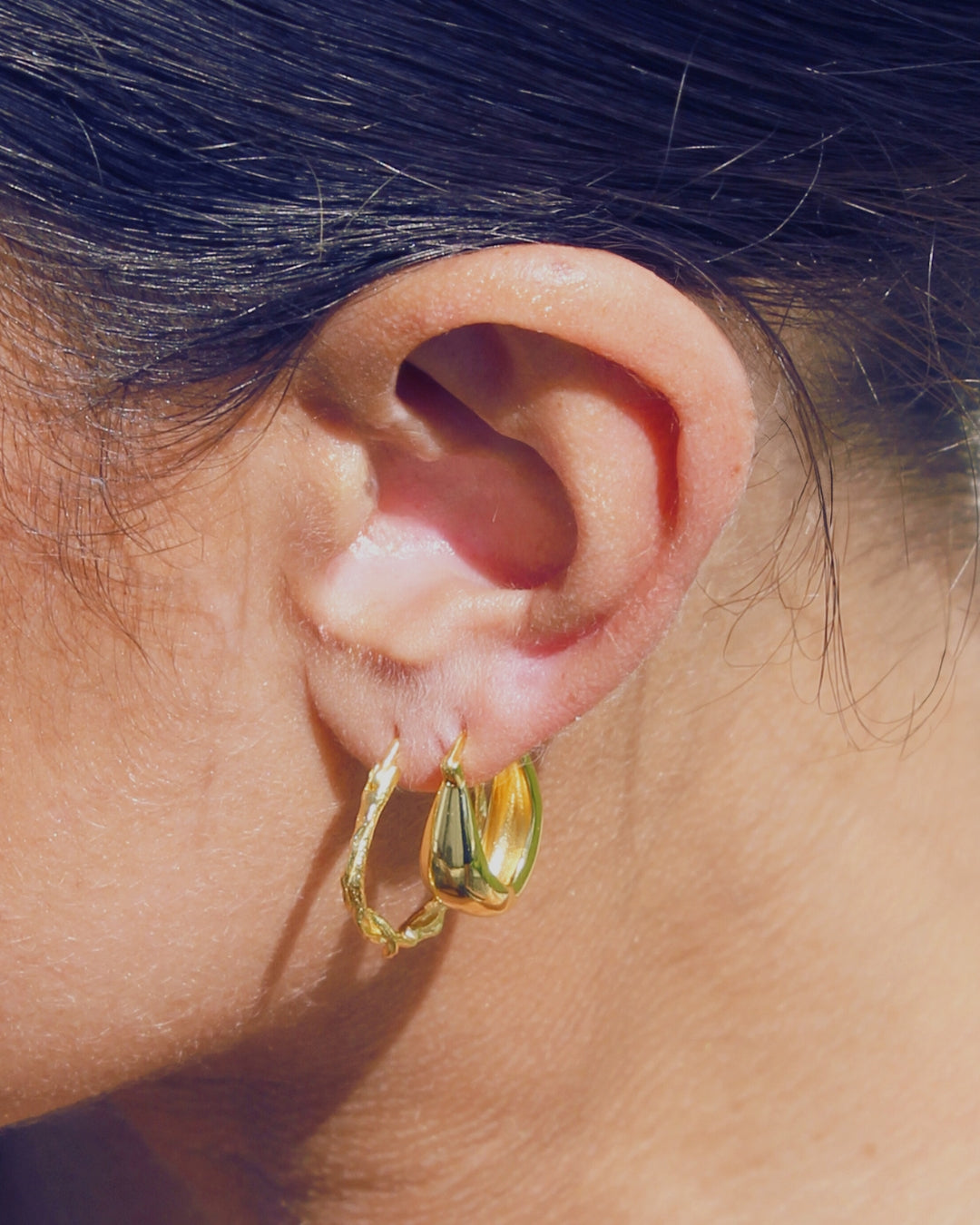 Gold hoop earrings worn by a person with dark hair.
