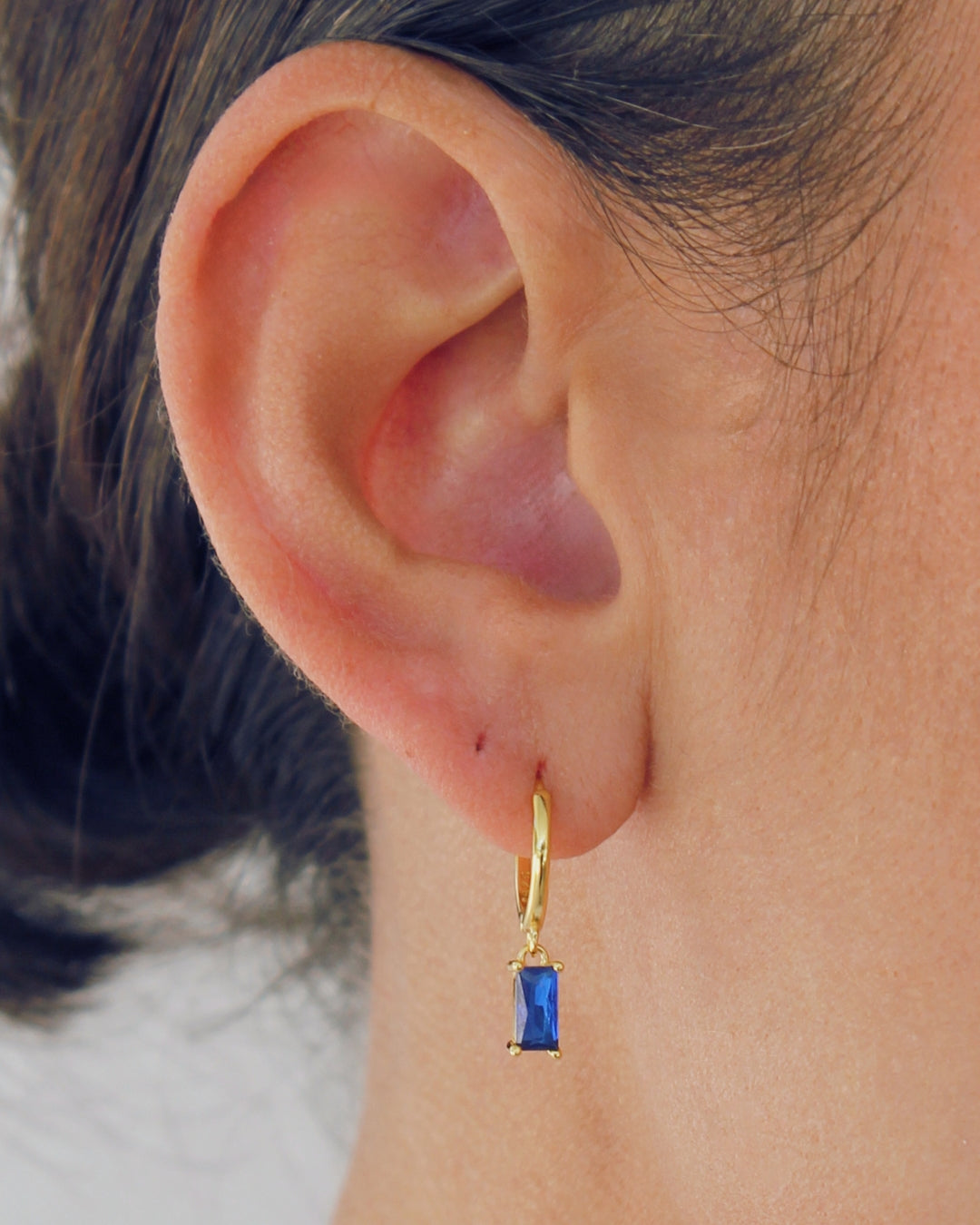 Close up of a bold pendant hoop earring with a blue gemstone worn by a person