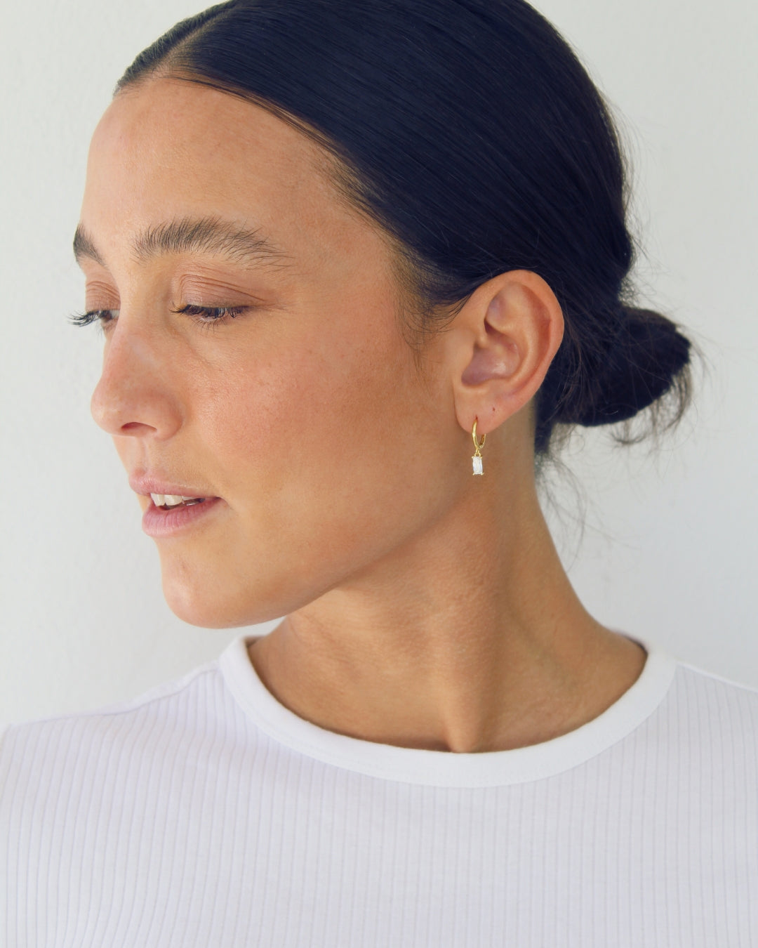 Woman wearing a gold pendant hoop earring against a plain background