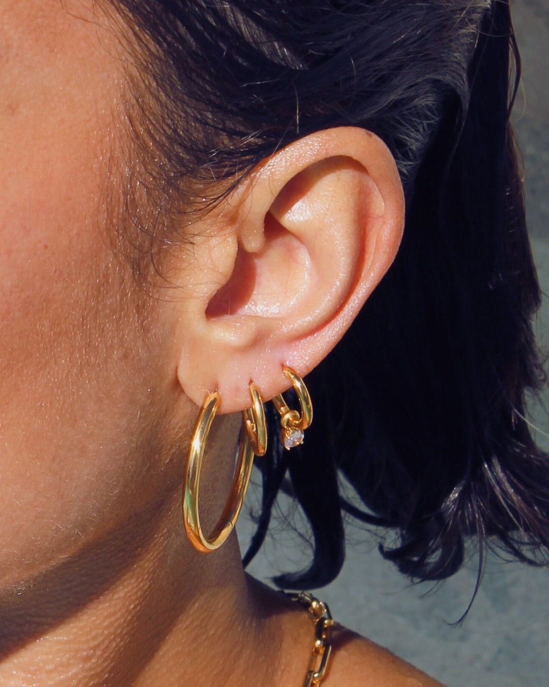 Close-up of an ear wearing gold pendant hoop earrings with clear gemstone