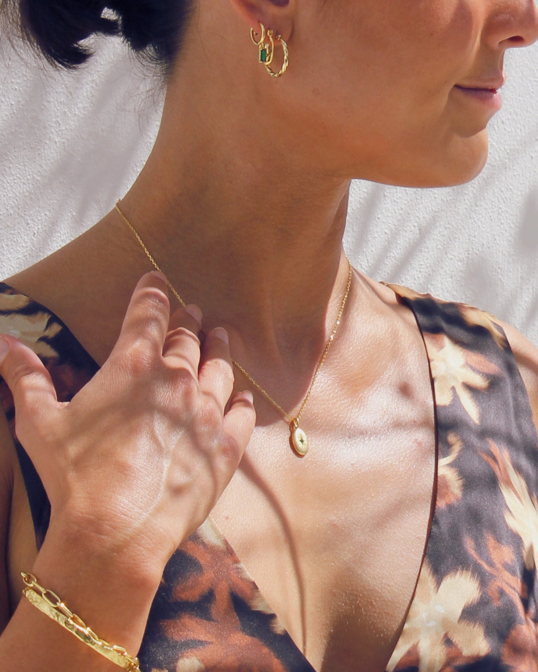Close-up of a woman wearing gold jewelry including an earring, necklace, and bracelet against a neutral background.