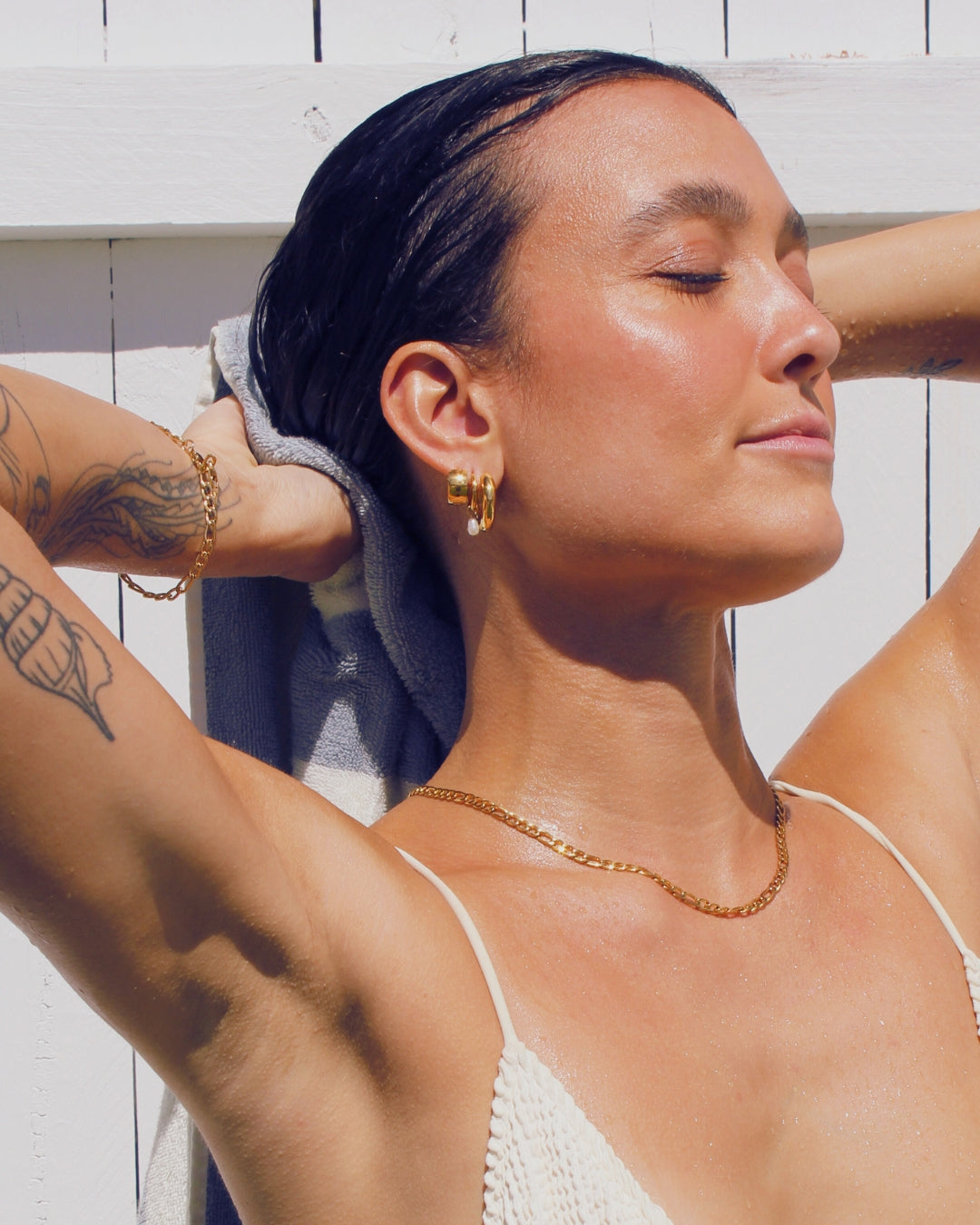 Woman with tattoos and gold jewelry against a white wooden background