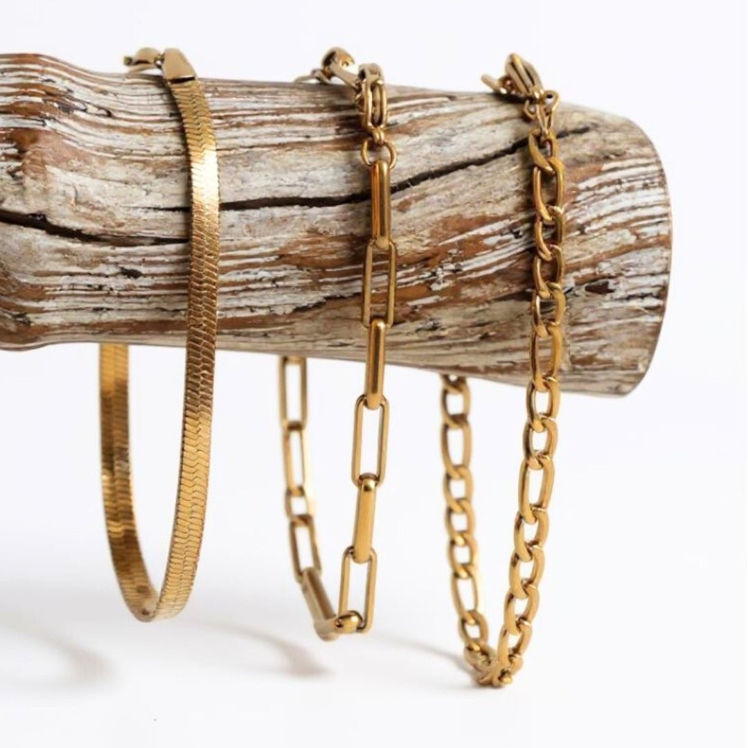 Three gold bracelets on a wooden log against a white background
