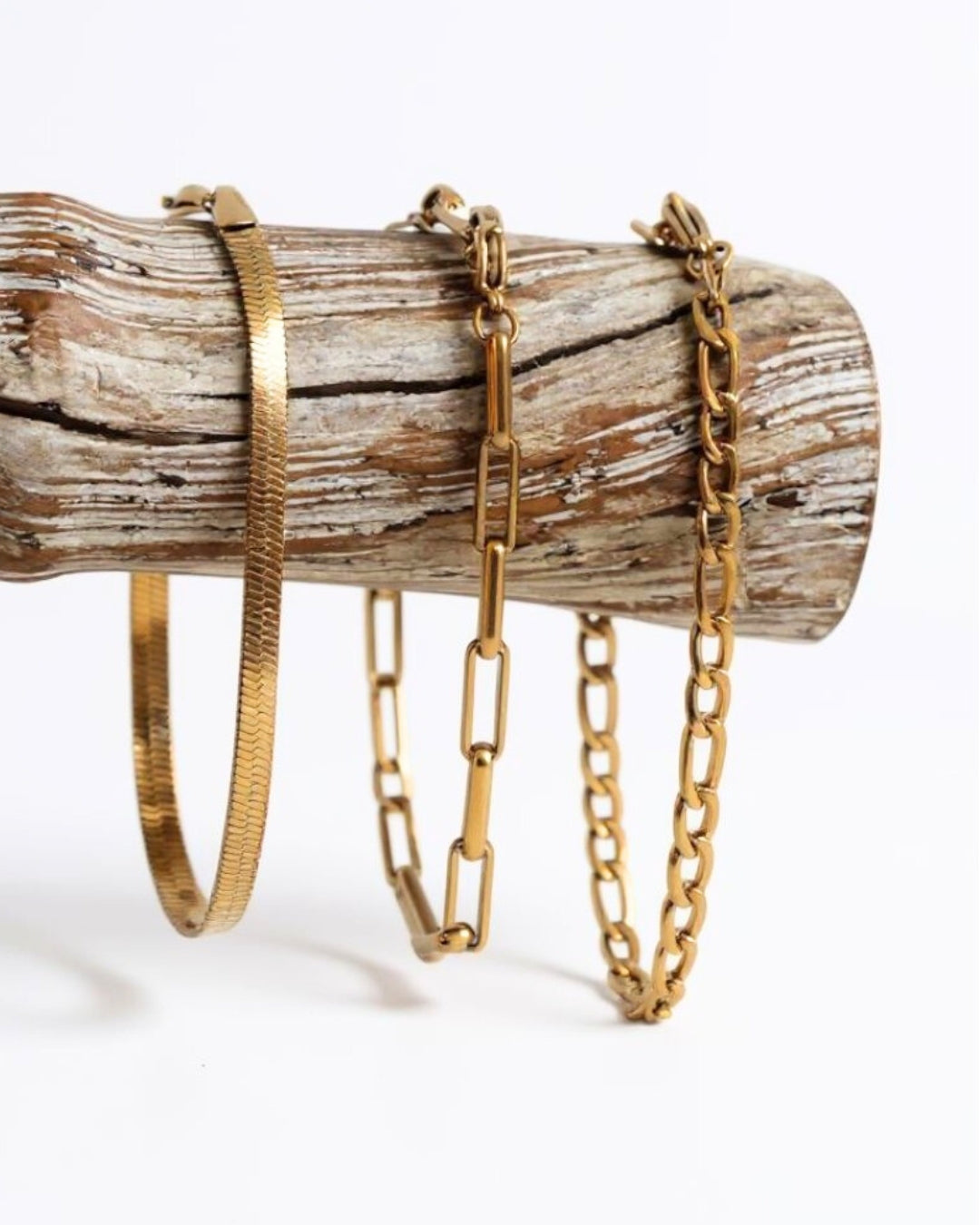 Three gold bracelets on a wooden log against a white background