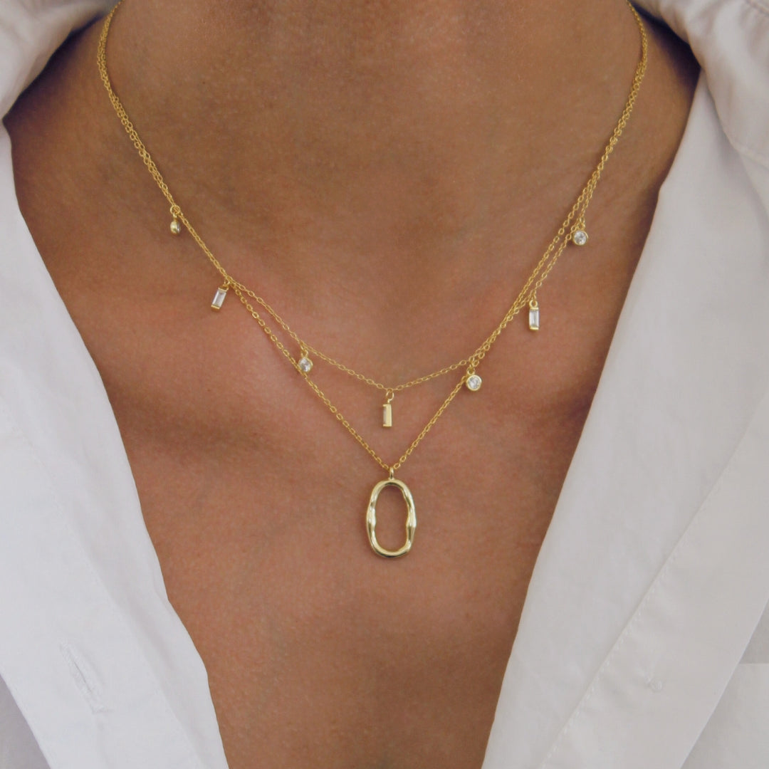 Gold necklace with a pendant on a person wearing a light-colored shirt.
