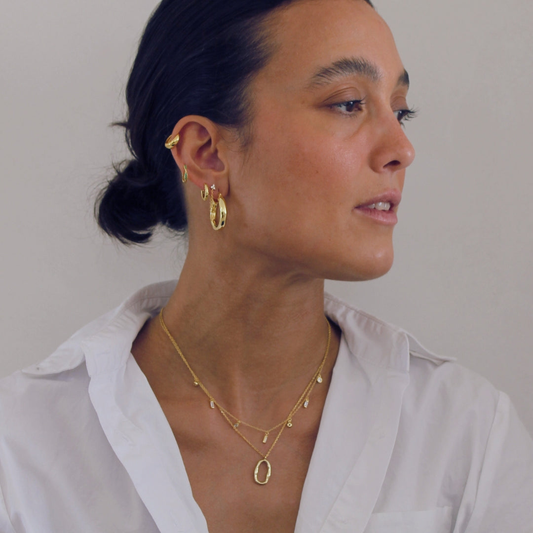 Woman wearing gold earrings and necklaces against a plain background