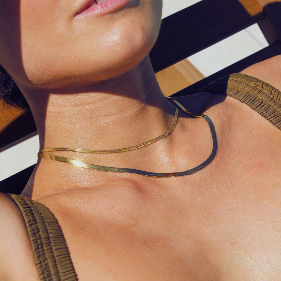 Close-up of a women wearing a 18k waterproof gold snake chain necklaces laying on a pool recliner