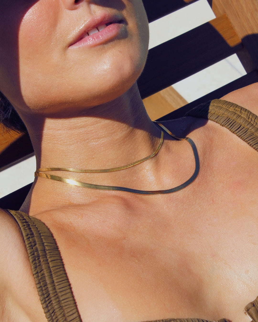Close-up of a women wearing a 18k waterproof gold snake chain necklaces laying on a pool recliner