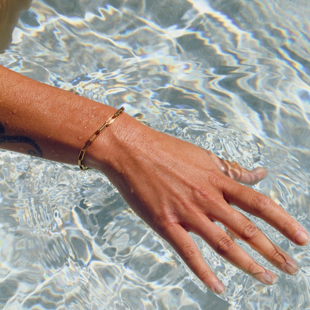 Hand with a gold paperclip bracelet in clear water