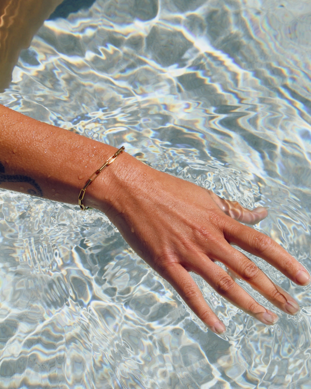 Hand with a gold paperclip bracelet in clear water