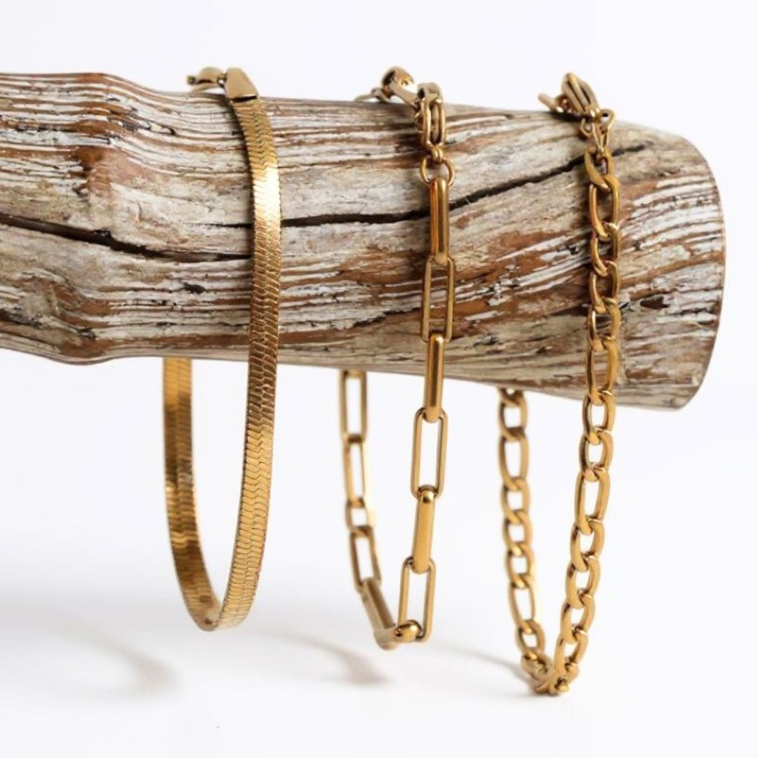 Three gold bracelets on a wooden log against a white background