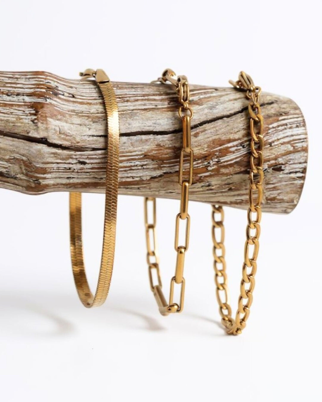 Three gold bracelets on a wooden log against a white background