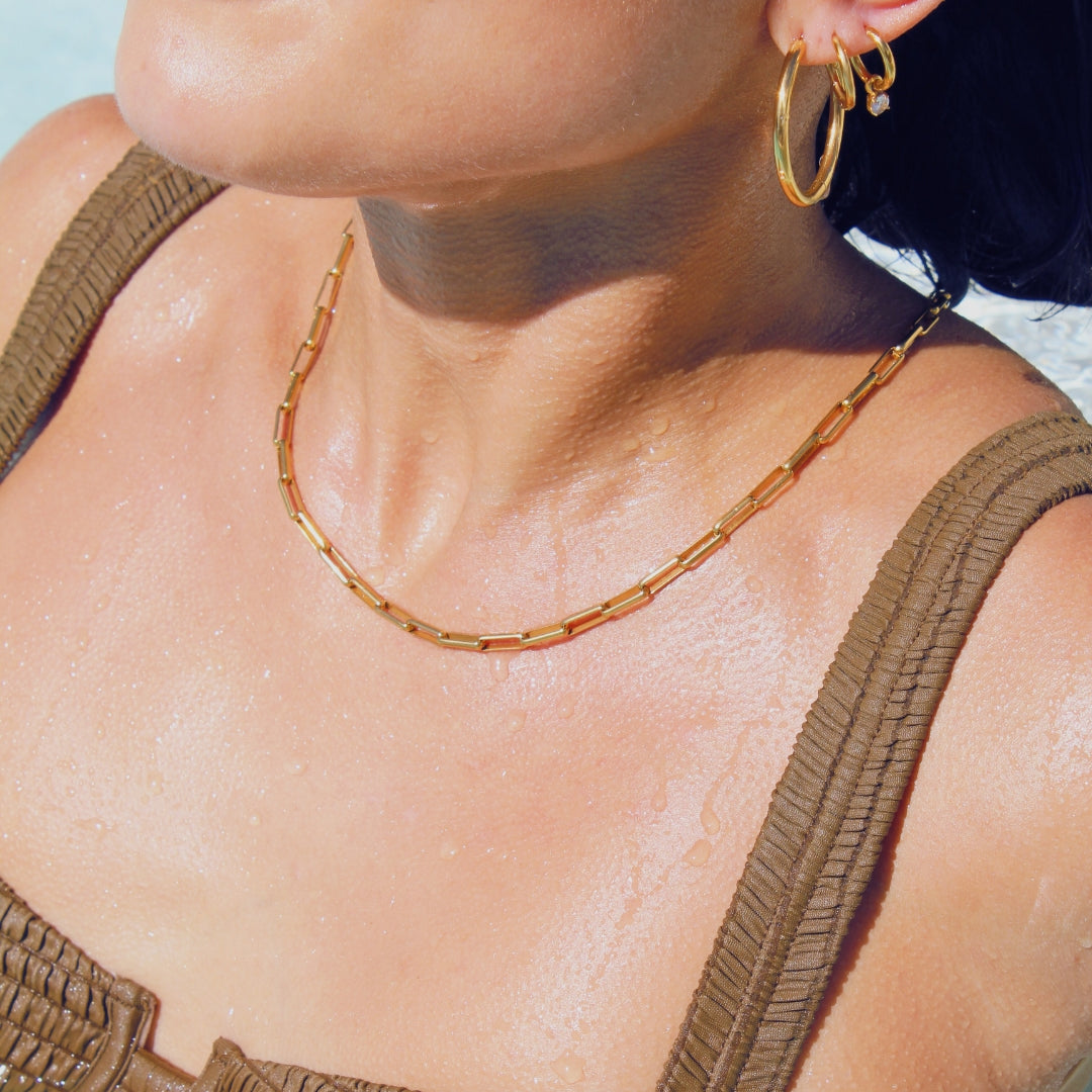 Close-up of a person wearing gold hoop earrings and a gold paperclip chain necklace in a pool