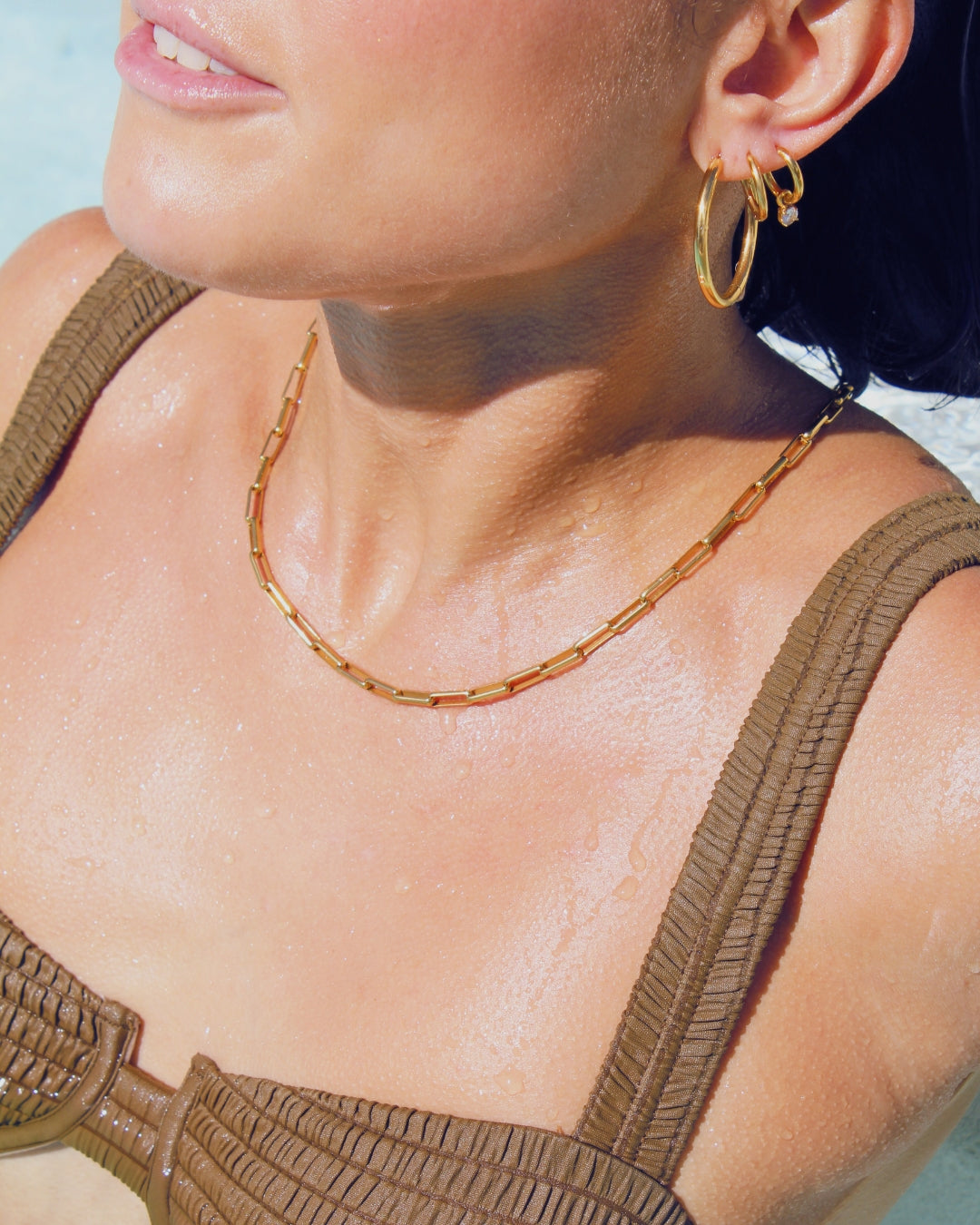 Close-up of a person wearing gold hoop earrings and a gold paperclip chain necklace in a pool