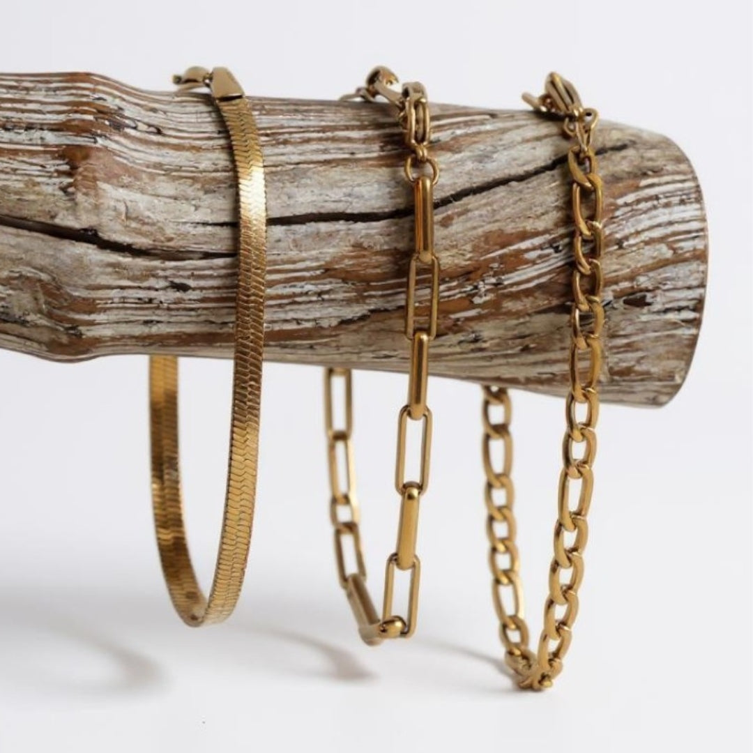 Three 18k waterproof gold bracelets on a wooden log against a white background