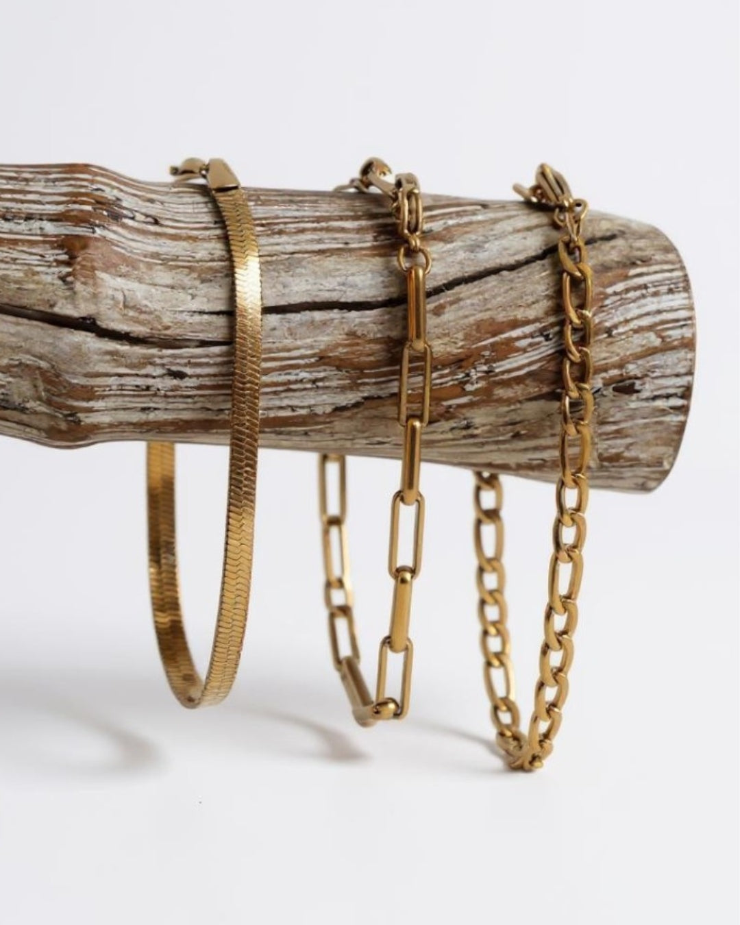 Three 18k waterproof gold bracelets on a wooden log against a white background