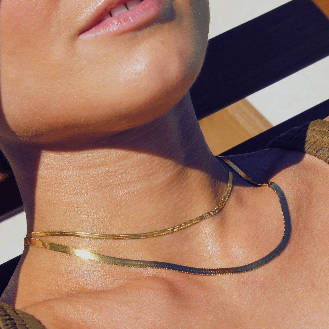 Close-up of a person wearing a gold snake chain necklace laying on pool recliner