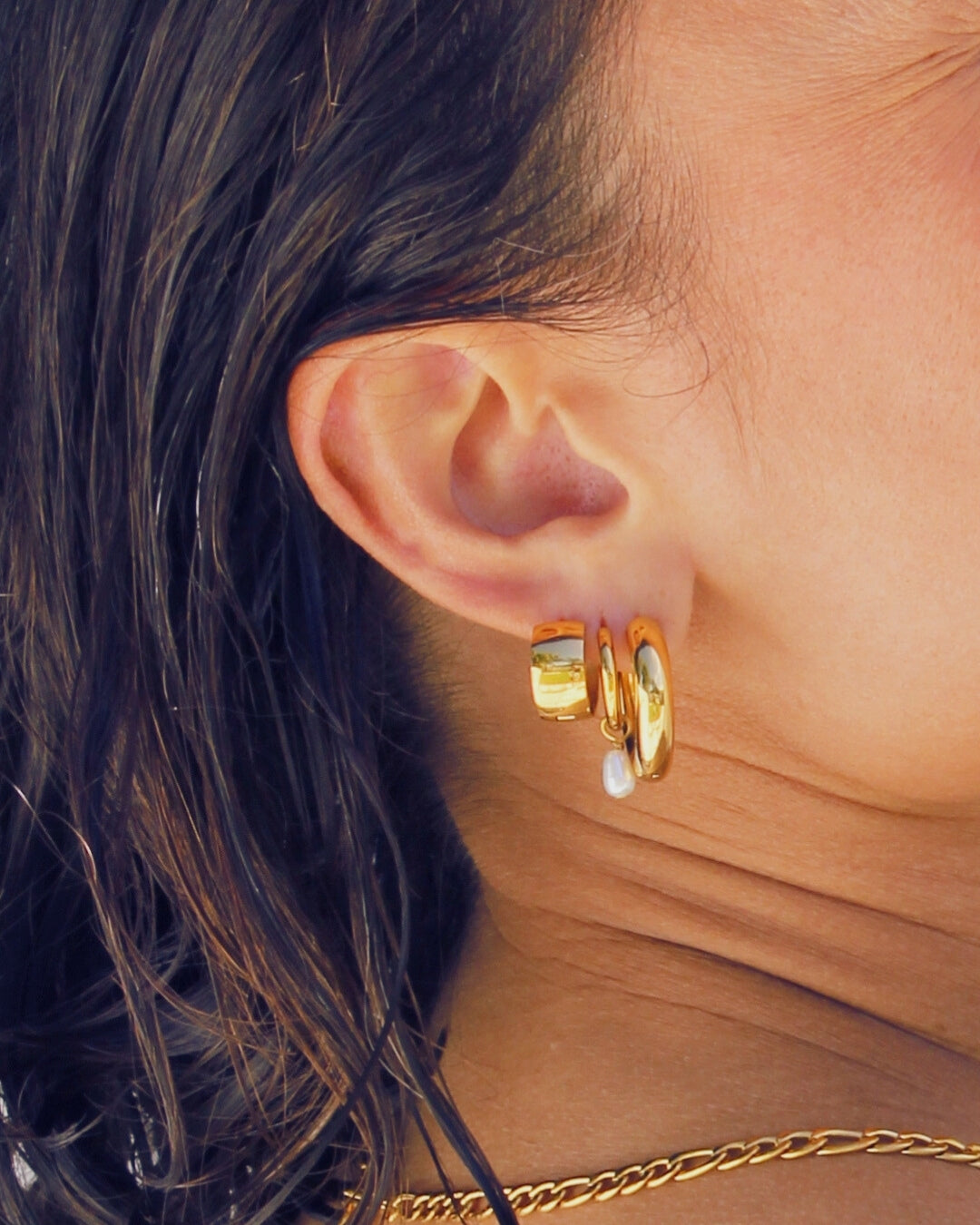Close-up of an ear wearing gold hoop earrings and a pearl drop earring