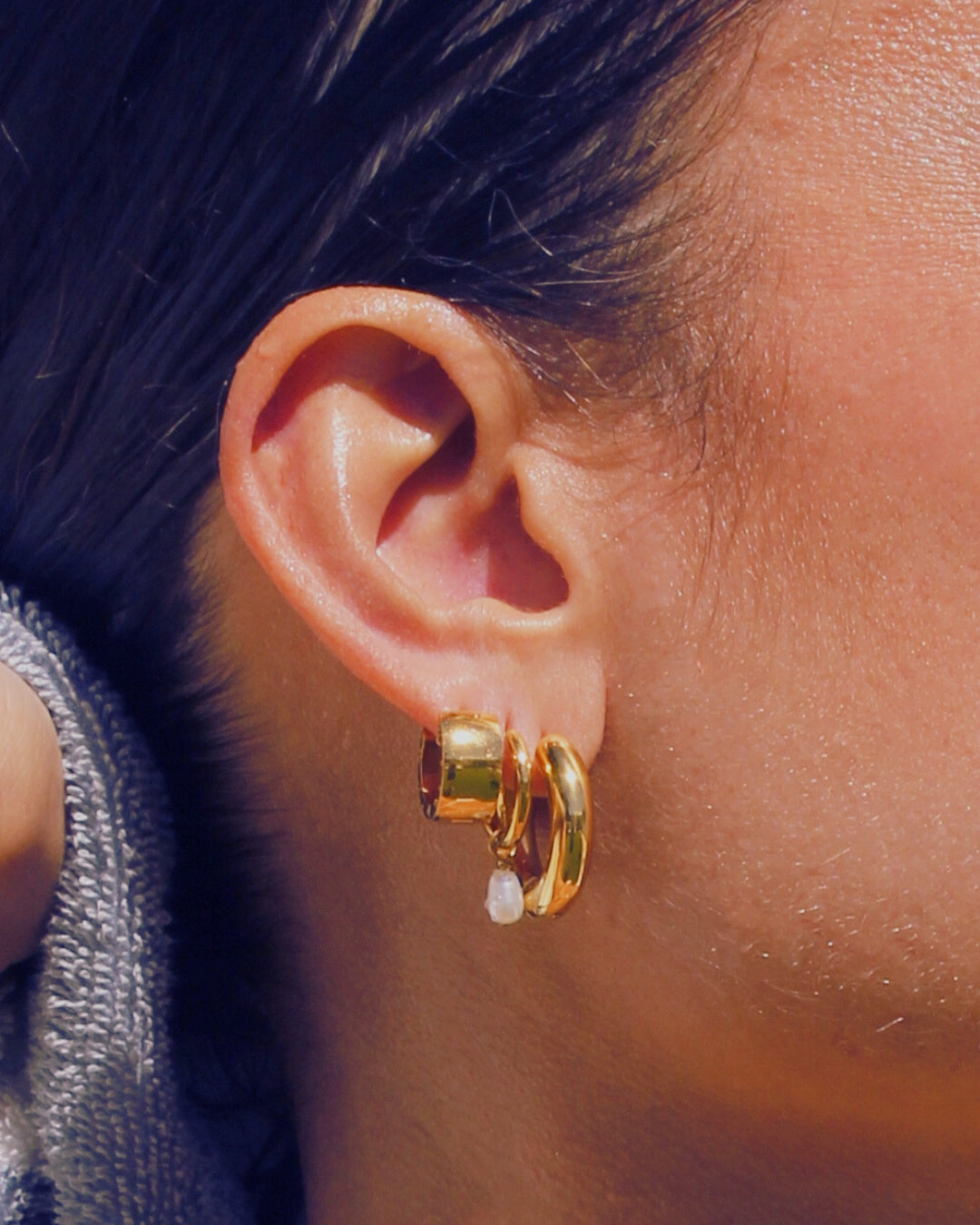Gold hoop earrings with a central pearl drop earring worn by a women.