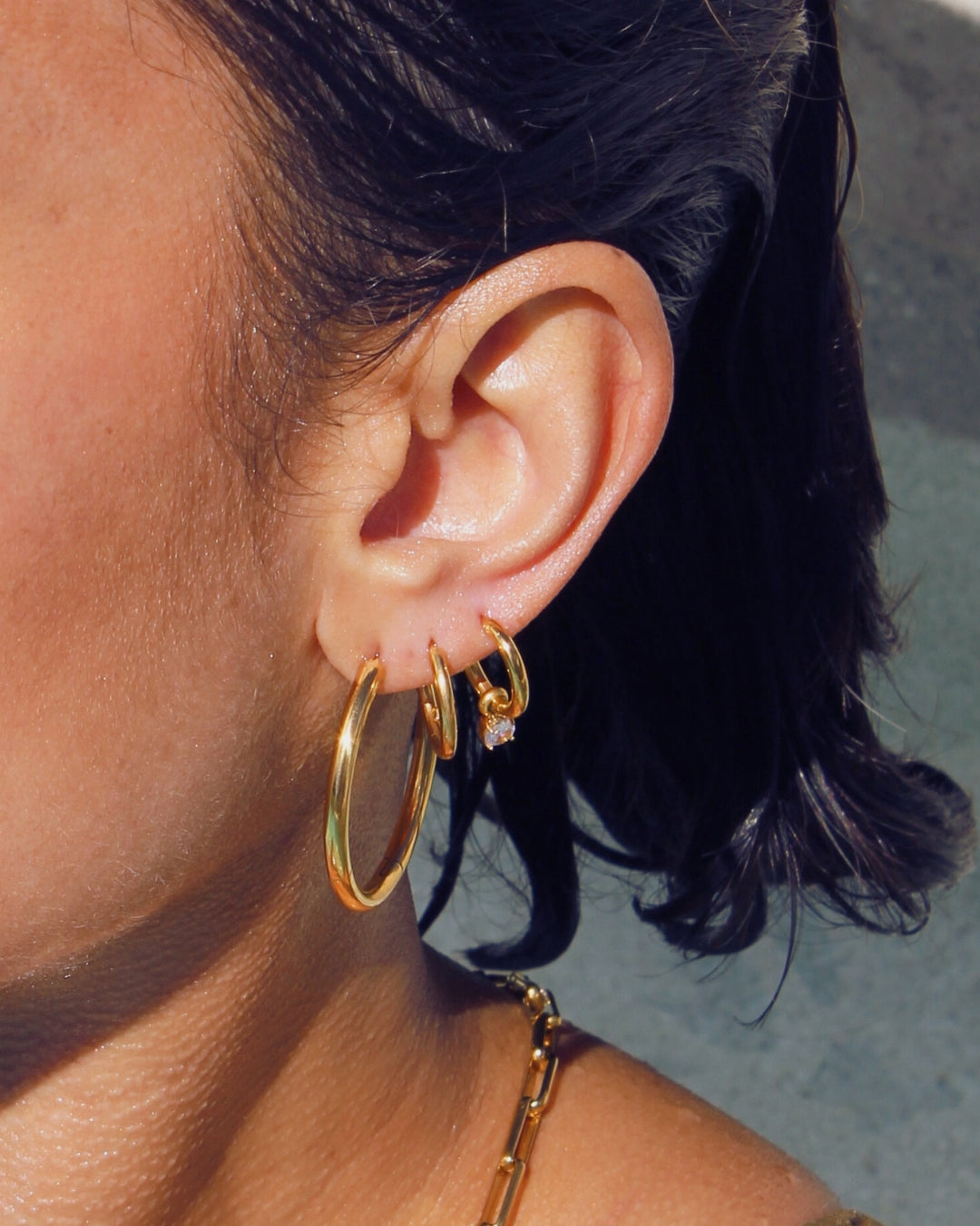 Close-up of an ear wearing waterproof gold hoop earrings with a blurred background