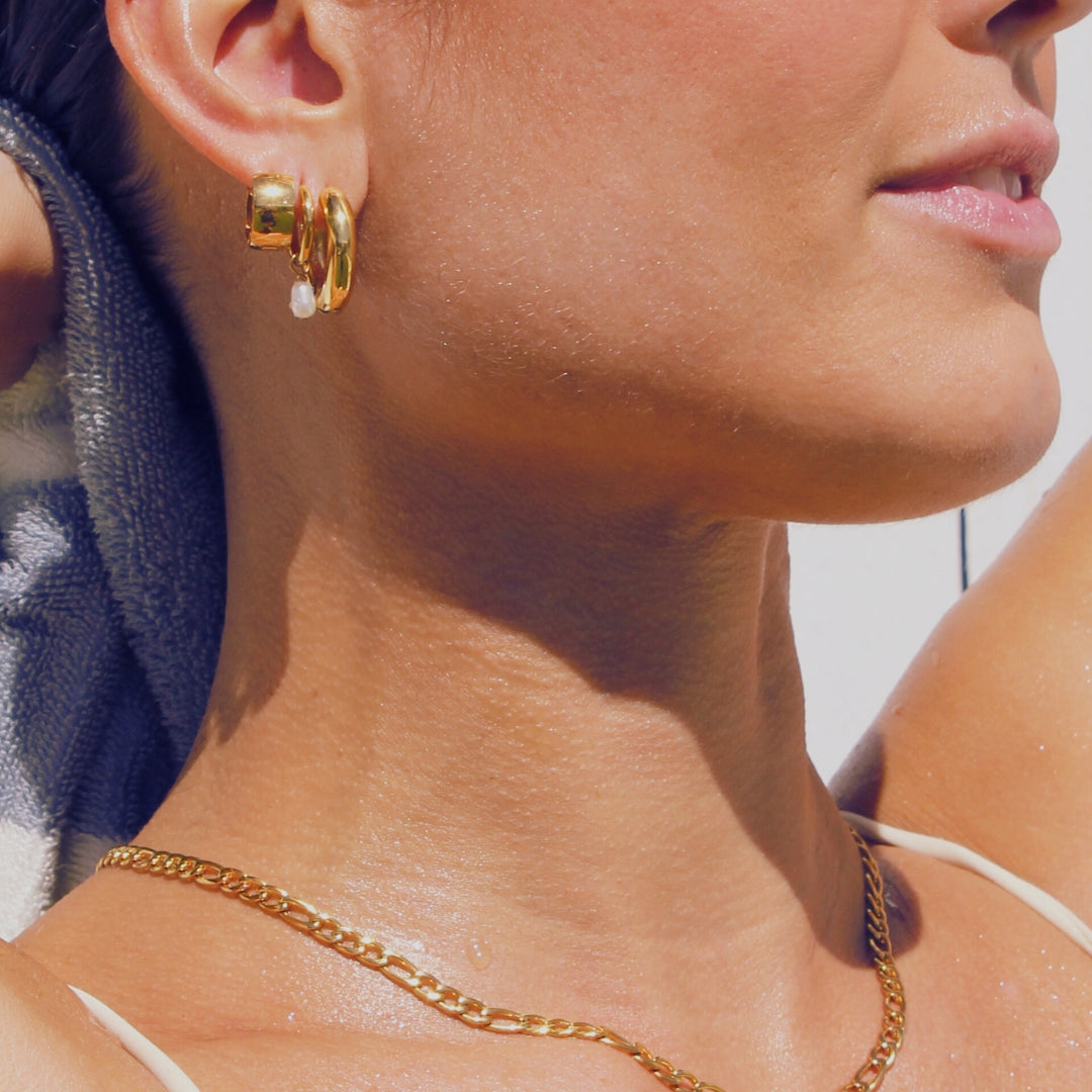 Close-up of a person wearing gold earrings and a gold figaro chain necklace.