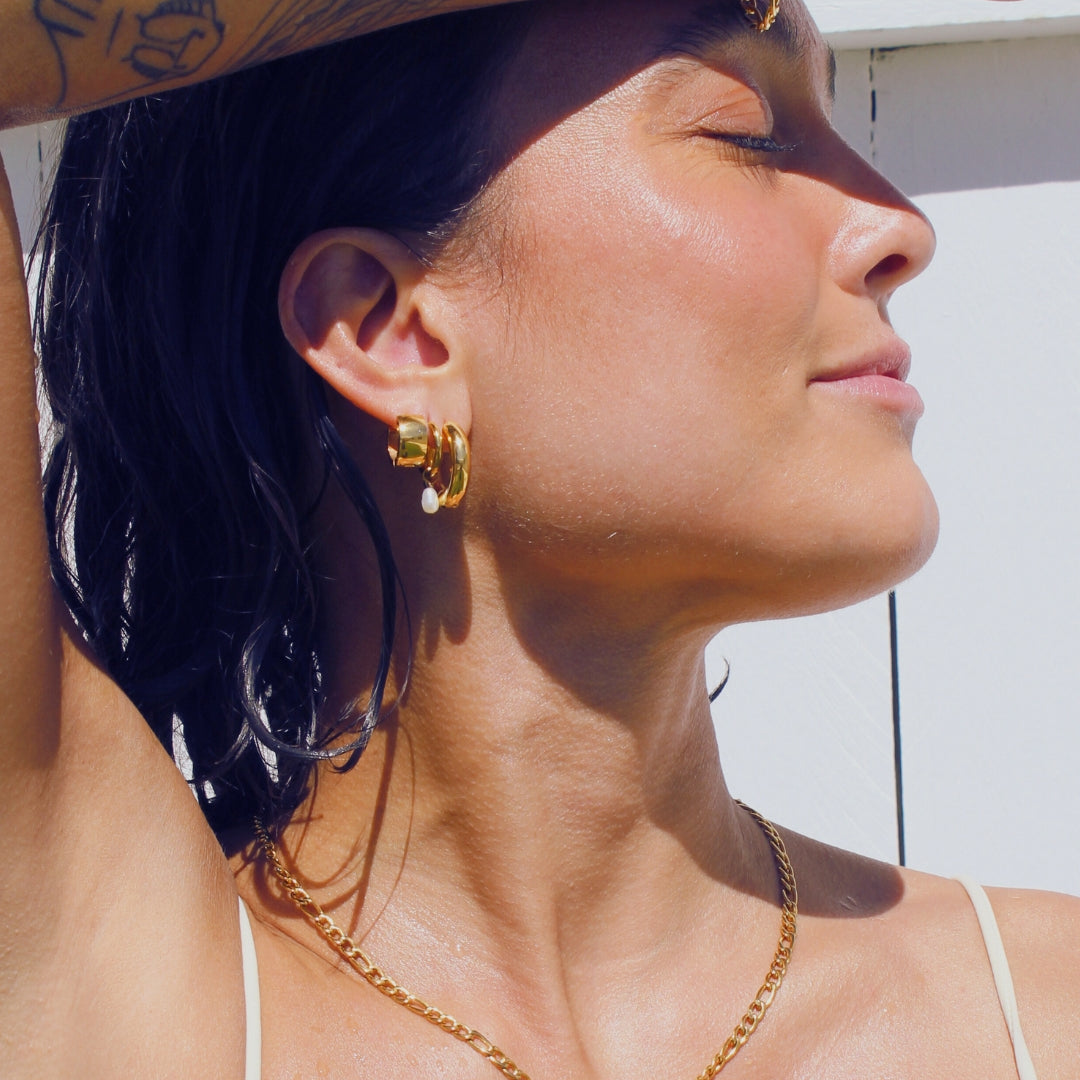 Woman with tattoos shielding her eyes from the sun, wearing gold waterproof jewellery.