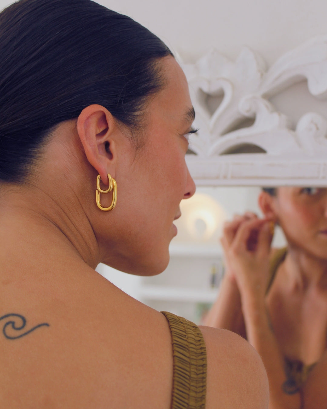 Person wearing gold hoop earrings looking in a mirror putting on more earrings